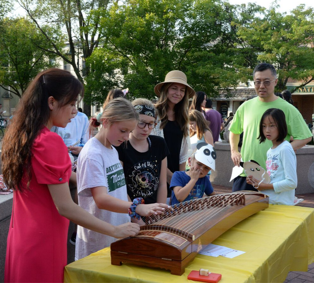 A woman helps children play a traditional instrument