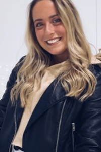 A photo of a girl with blond hair, wearing a black jacket and tan shirt