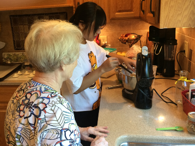 a student cooks while an older woman stands and watches her