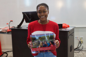 a girl stands and holds a sheet which says she won a $1000 study abroad scholarship