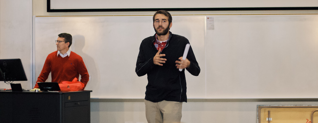 a student presents and stands in the front of the room, talking with his hands