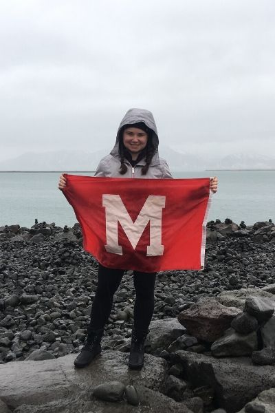 Abigail Gabler holds a Miami flag while standing on a rocky surface