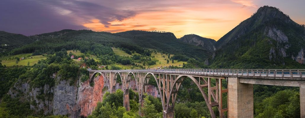 a bridge sits in the mountains with a sunset in the background