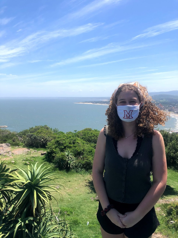 Anna wears a Miami facemask while standing in front of beautiful scenery in Uruguay