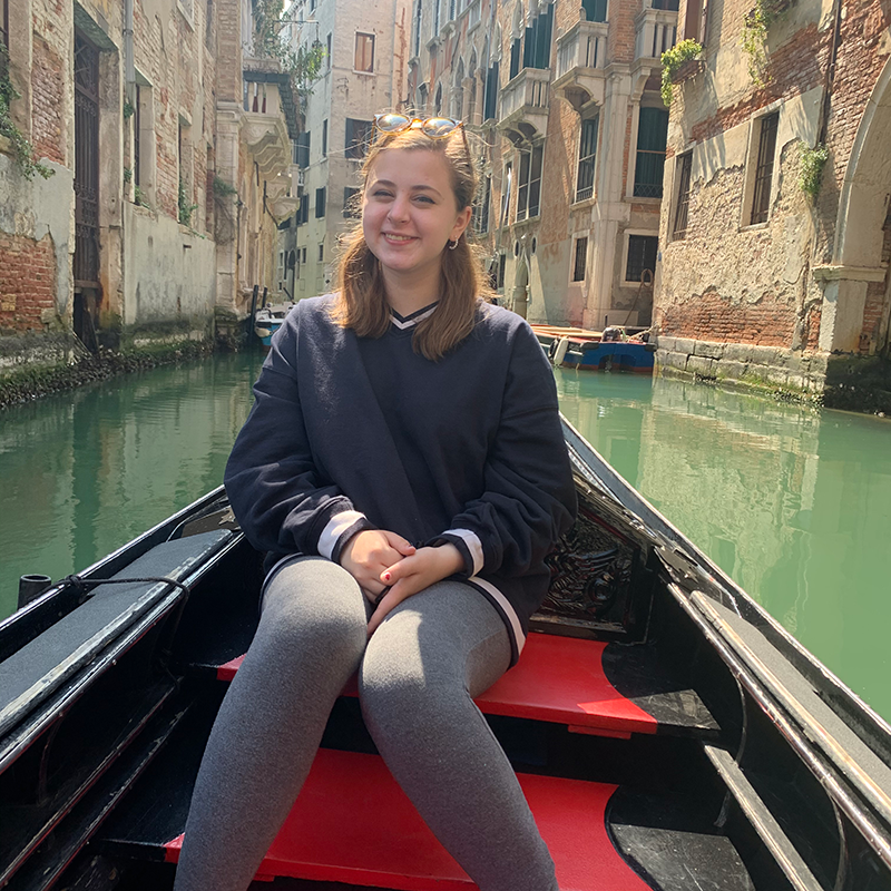 Paige sits in a canal boat with buildings and canal in background