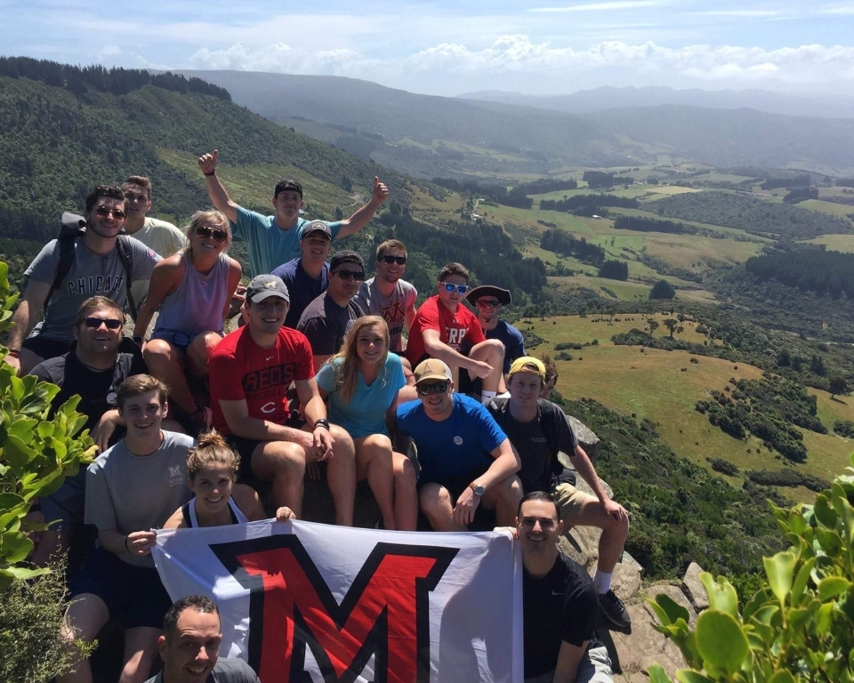 a study abroad group poses with a Miami flag on mountainside