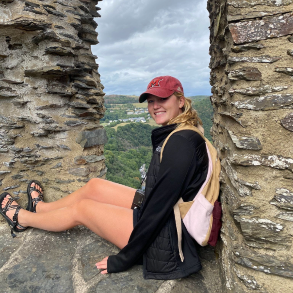 Gracie sits with outstretched legs against a stone wall, with countryside in background