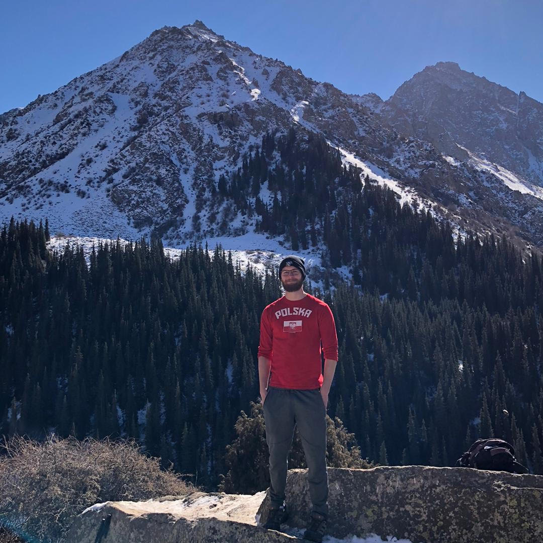 Colton stands outdoors in Kyrgyzstan, with snow-capped mountains visible in the background