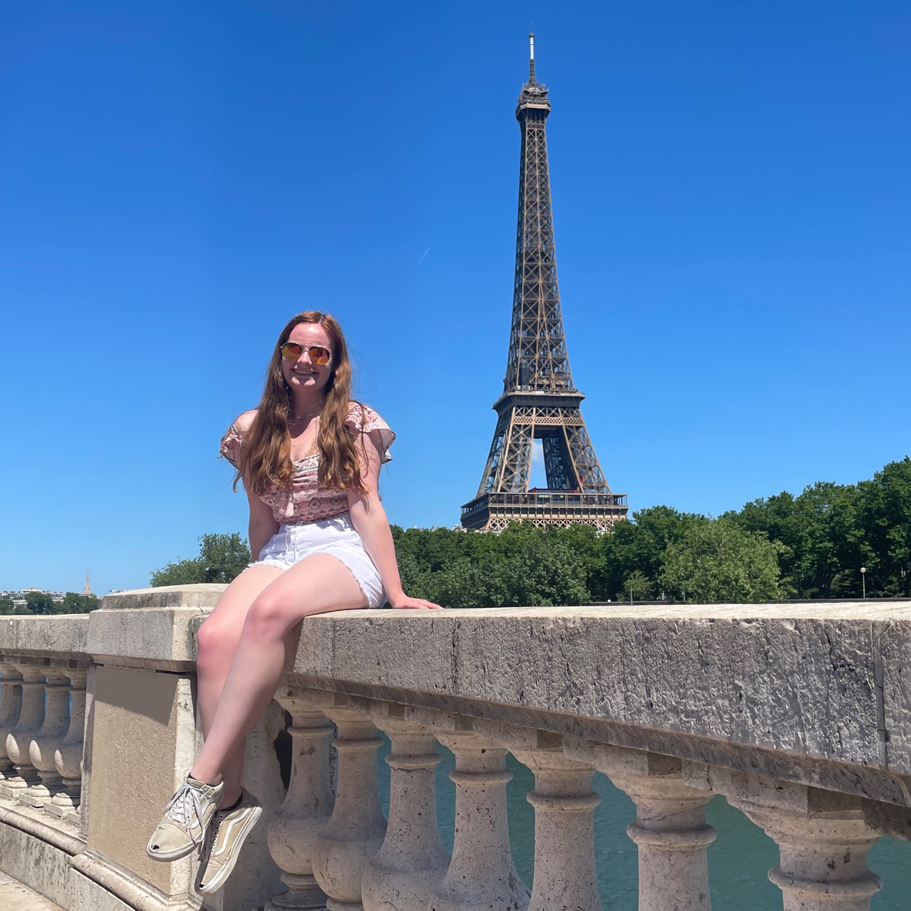 Hannah sits on a low concrete wall. The Eiffel Tower is visible in the background