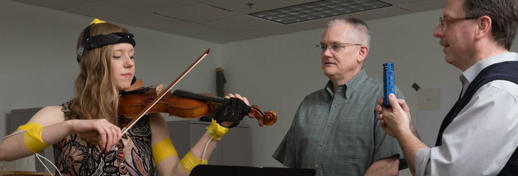 Female student playing violin while electrodes are on her arms 