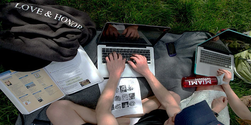 Hands poised above a laptop on the ground outside, viewed from above