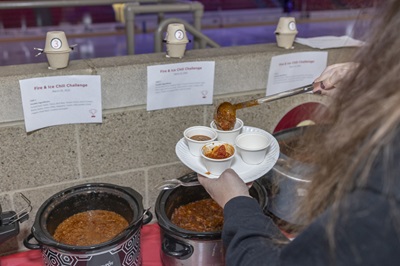 A person taking scoops of chili out of a crock pot