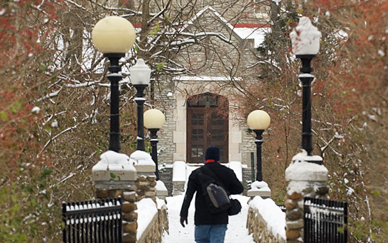 A student walks on a pathway in the winter, with snow all around