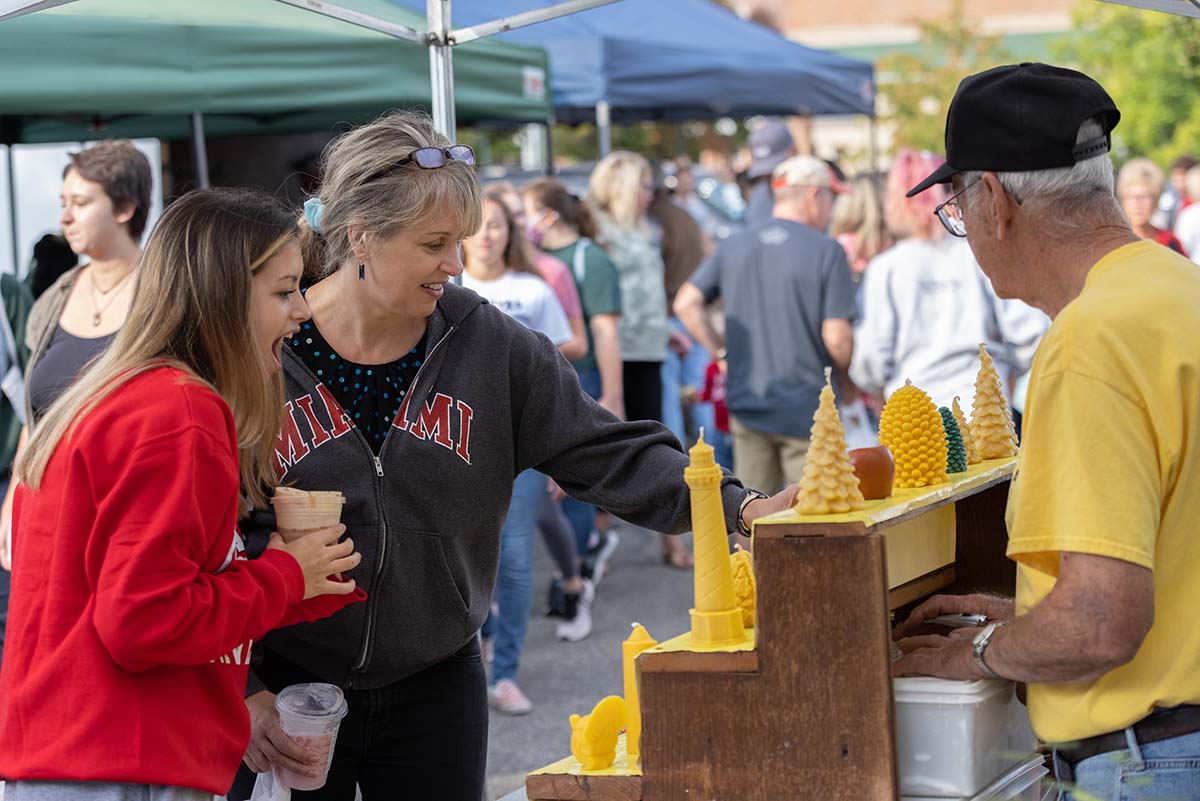 Two women admiring beeswax candles at a booth at the Oxford Farmer's Market.
