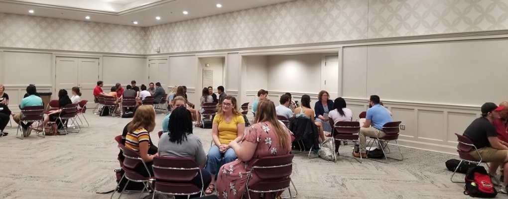 Several tables with groups of 6-8 RAs with a facilitator during RA Training