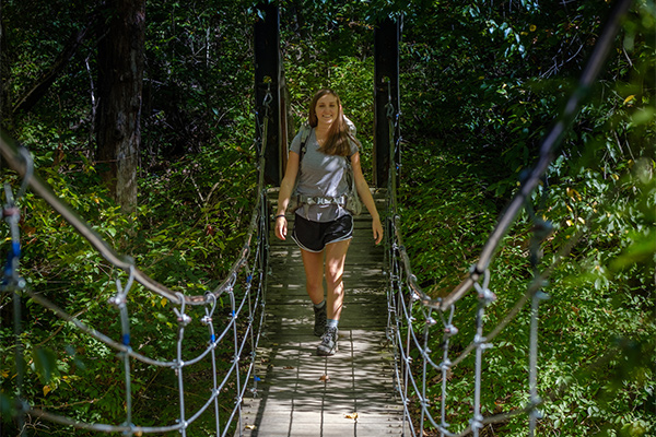student hiking across a hanging bridge in the natural areas