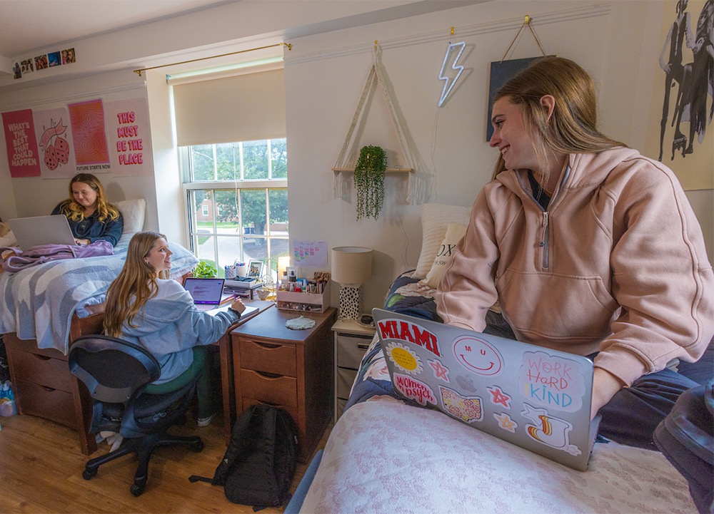 Students in their dorm room posing with plants for a selfie.