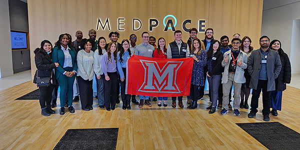 PCLS participants pose for a picture with a Miami University flag in front of a Medpace logo.