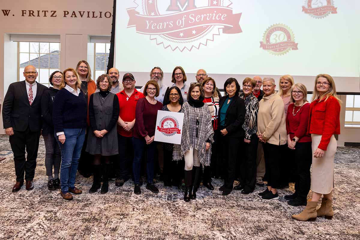 25 years of service groups poses in front of a screen