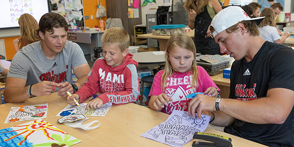 Miami University baseball players David Novak, left, and Dominic Krupinski, far right, help Kramer Elementary students Christian Smiley, second from left, and Alexis Hinson during art class.
