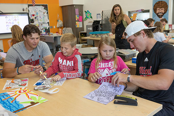 Miami University baseball players David Novak, left, and Dominic Krupinski, far right, help Kramer Elementary students Christian Smiley, second from left, and Alexis Hinson during art class.