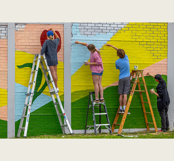 Students stand on ladders to paint the mural on a wall facing Spring Street. “We had 12-14 sessions on this that were two hours at a time,” said Michael Stillion, associate professor of Studio Art.