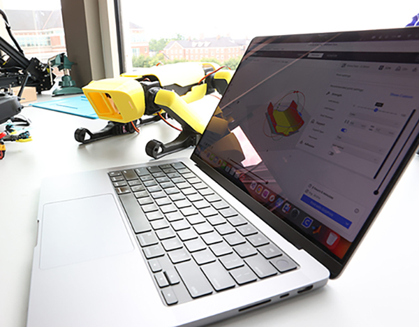 a laptop open on a table with a small yellow doglike robot next to it
