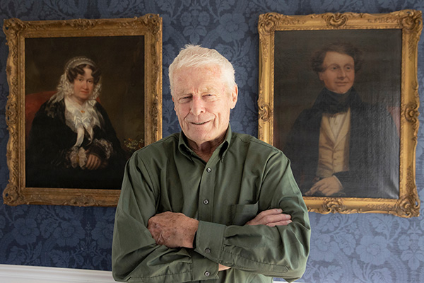 Richard Cocks stands in his Indian Hill home between the two first paintings he purchased. They are mid-19th century paintings of a man and a woman (photo by Jeff Sabo).