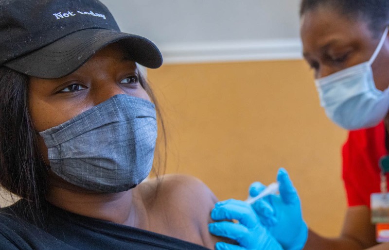 Zainab Soumahoro receives the vaccine while wearing a mask and a hat that says Not Today