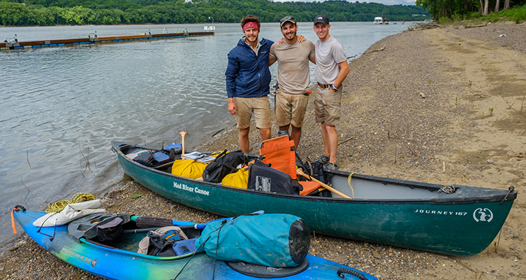 Jackson, Quinton, and Tyler stand on the river shore by their canoe and kayak