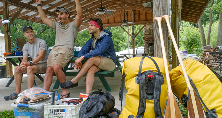 The guys talk under a camp shelter