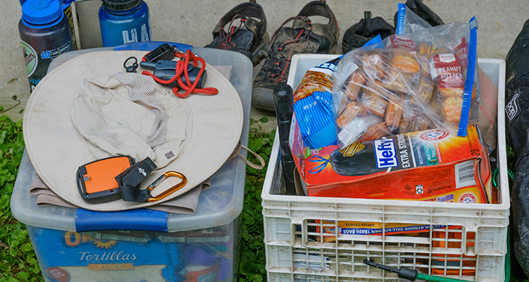  Bins packed full of supplies like tortillas, packages of peanut butter grackers, a whistle, garbage bags, water bottles, a sun hat, a walkie talkie, and a compass.