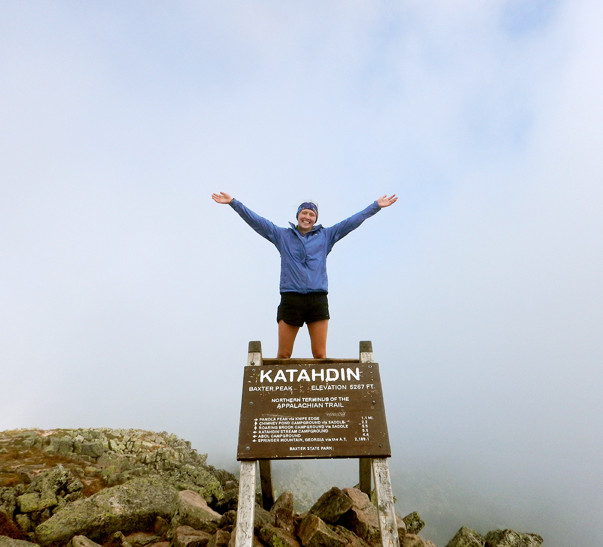 Tess stands with her arms raised on the top of Mount Katahdin