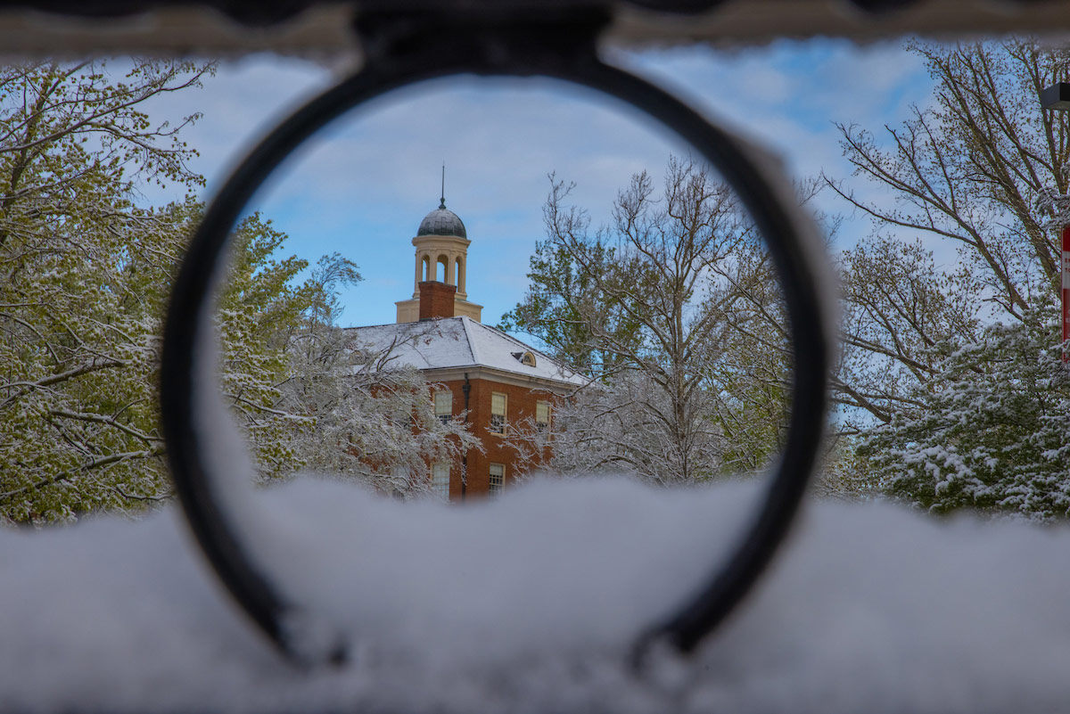 Snow in spring: Looking outside through a circle in the window of the front of Kreger Hall frames a view of snow -covered trees and the cupola on top of Wells Hall.
