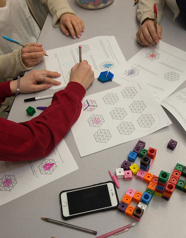 Arm and hand of a person drawing shapes on paper, with cubes and iPad in foreground