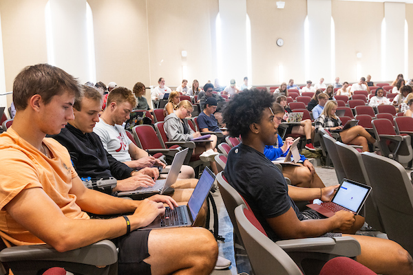 A large group of students sit in a lecture hall.