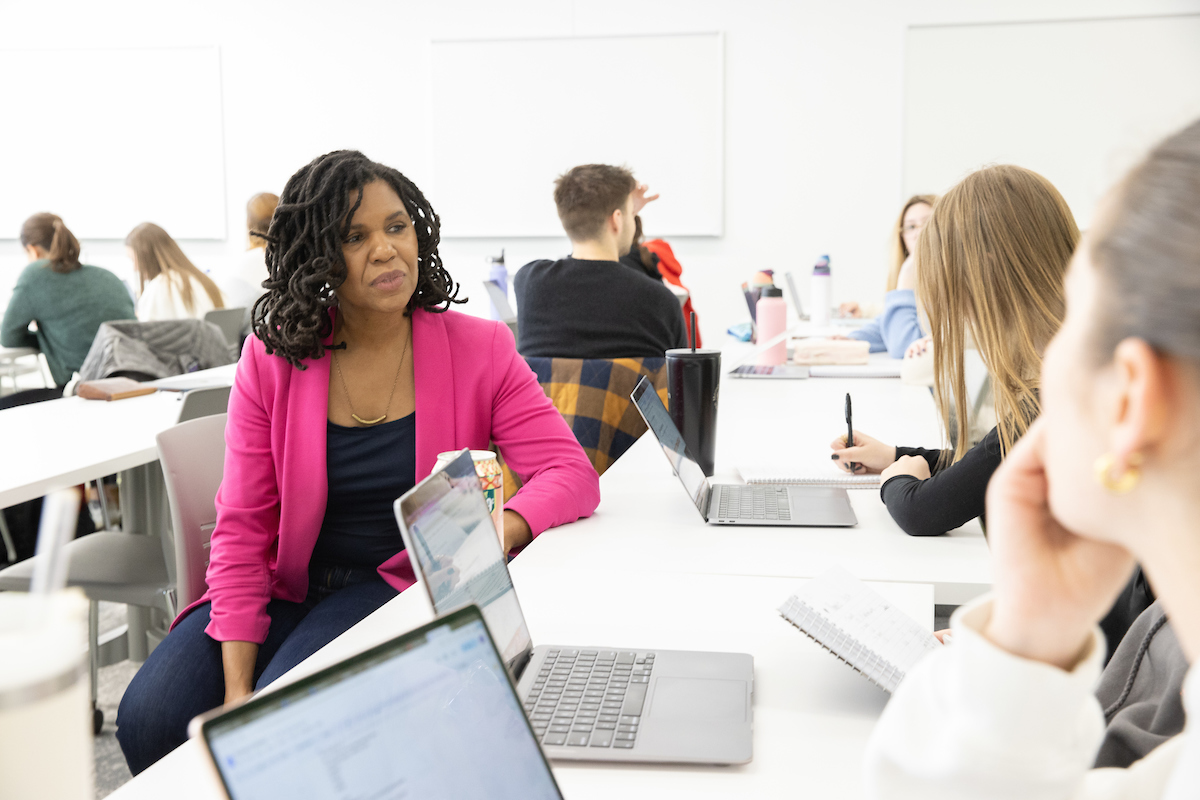 A professor talks with a student while sitting at a desk.