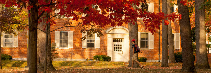 Student walking down sidewalk under orange fall leaves