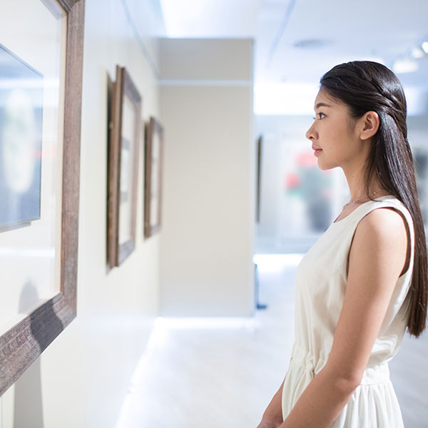 A female looking at a piece of artwork on the wall. 