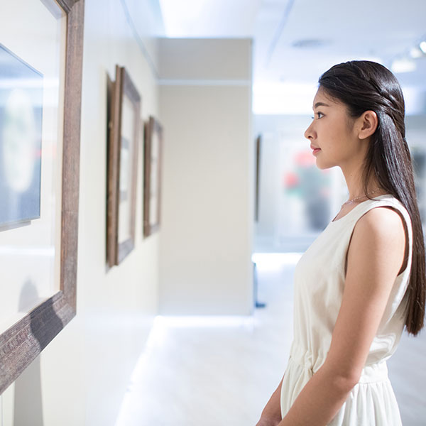 A female looking at a piece of artwork on the wall.