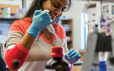 A student in a lab using a pipet to extract liquid from a small tube.