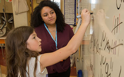 A student teacher helping a student write on the white board.