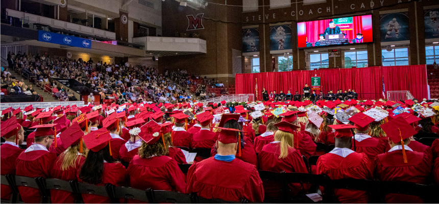 Graduates seated before the stage, a field of Miami red caps and gowns.