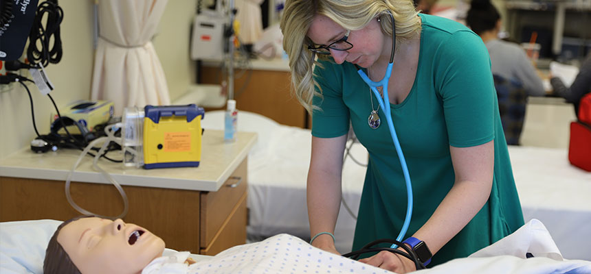  A female nursing student working on a simulation mannequin with a stethoscope in her ears