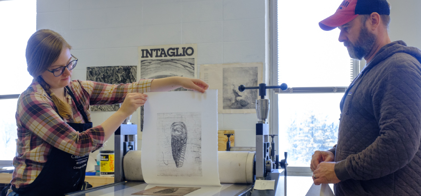 Student looking at her printmaking piece with her professor. 