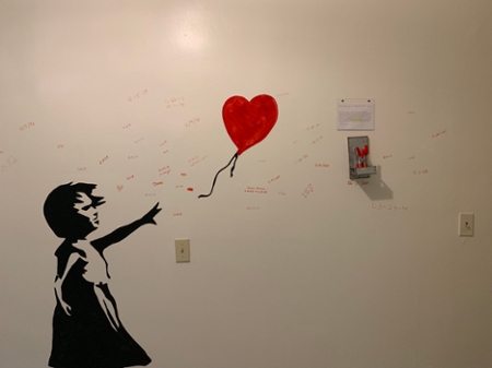 A painting of a silhouette of a girl chasing a red balloon.  