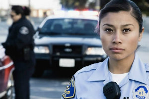 Female law officer standing with her arms crossed at her chest and a police car in the background.