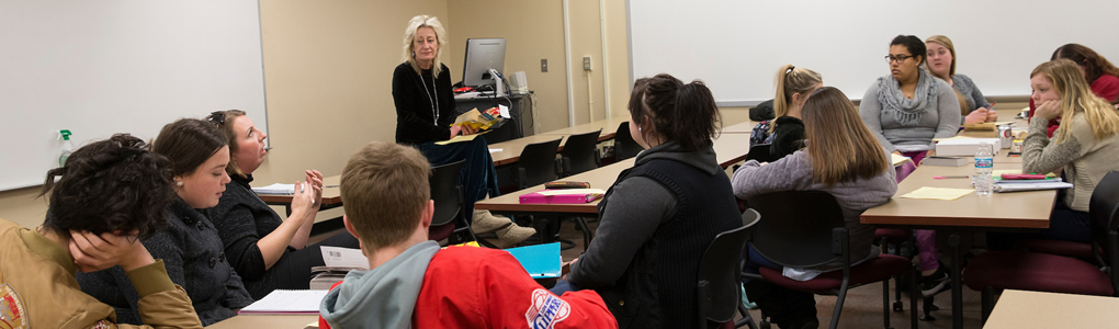  Professor Diana Royer standing in the front of the classroom teaching to her students.
