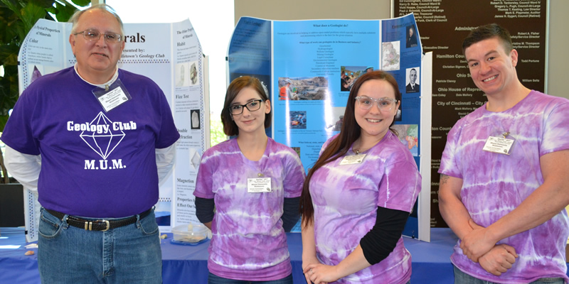  Four members of the MUM Geology Club stand in front of their information table at GeoFair.
