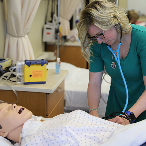 A students working on the simulation manikin with her stethoscope.